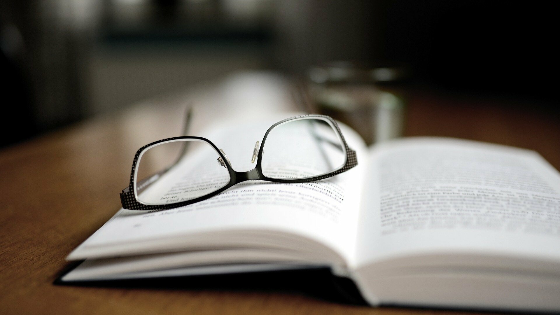 Ein aufgeklapptes Buch, auf dem eine Brille liegt.