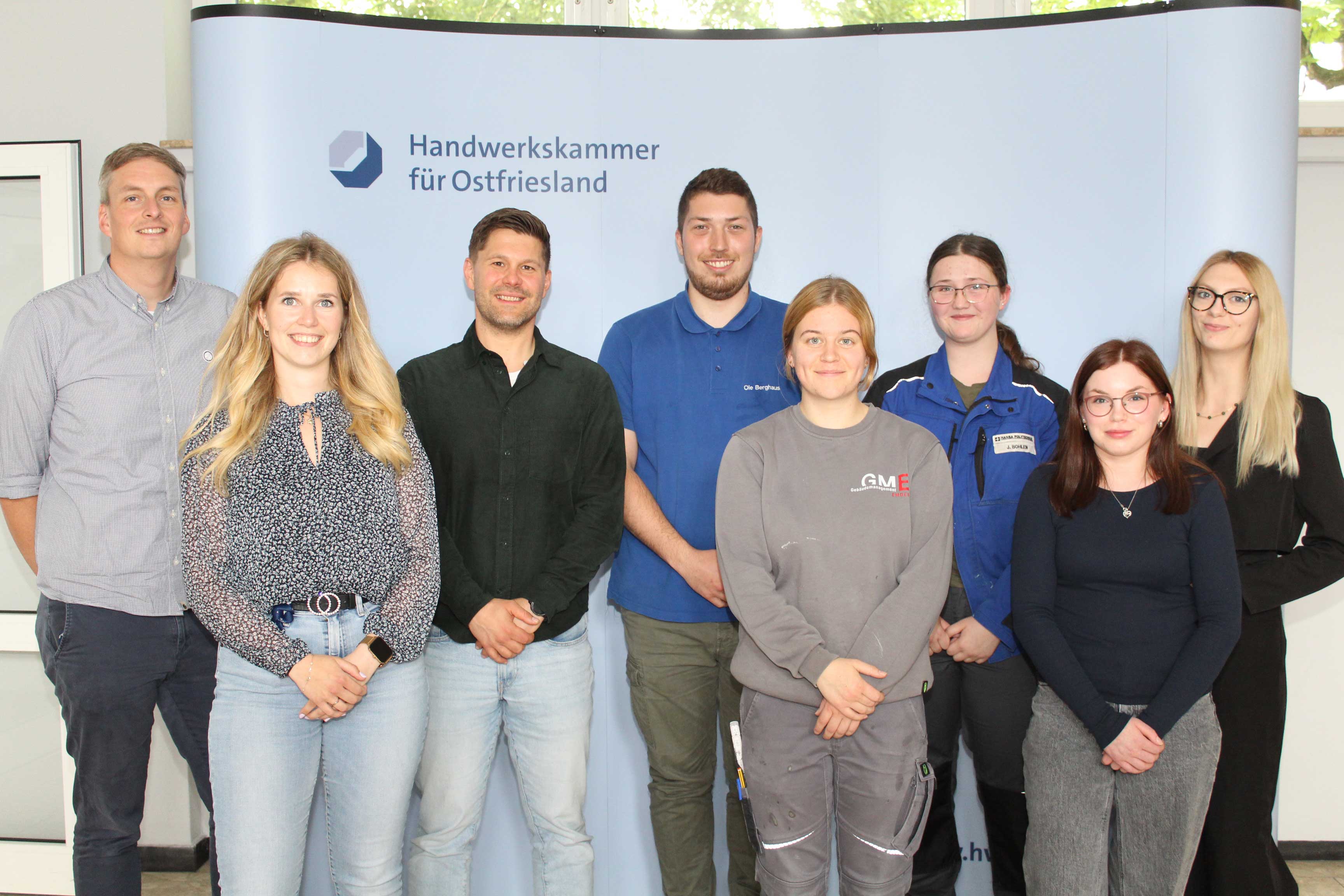 KI generiert: Eine Gruppe von acht Personen steht vor einem Hintergrund mit dem Logo der Handwerkskammer für Ostfriesland.