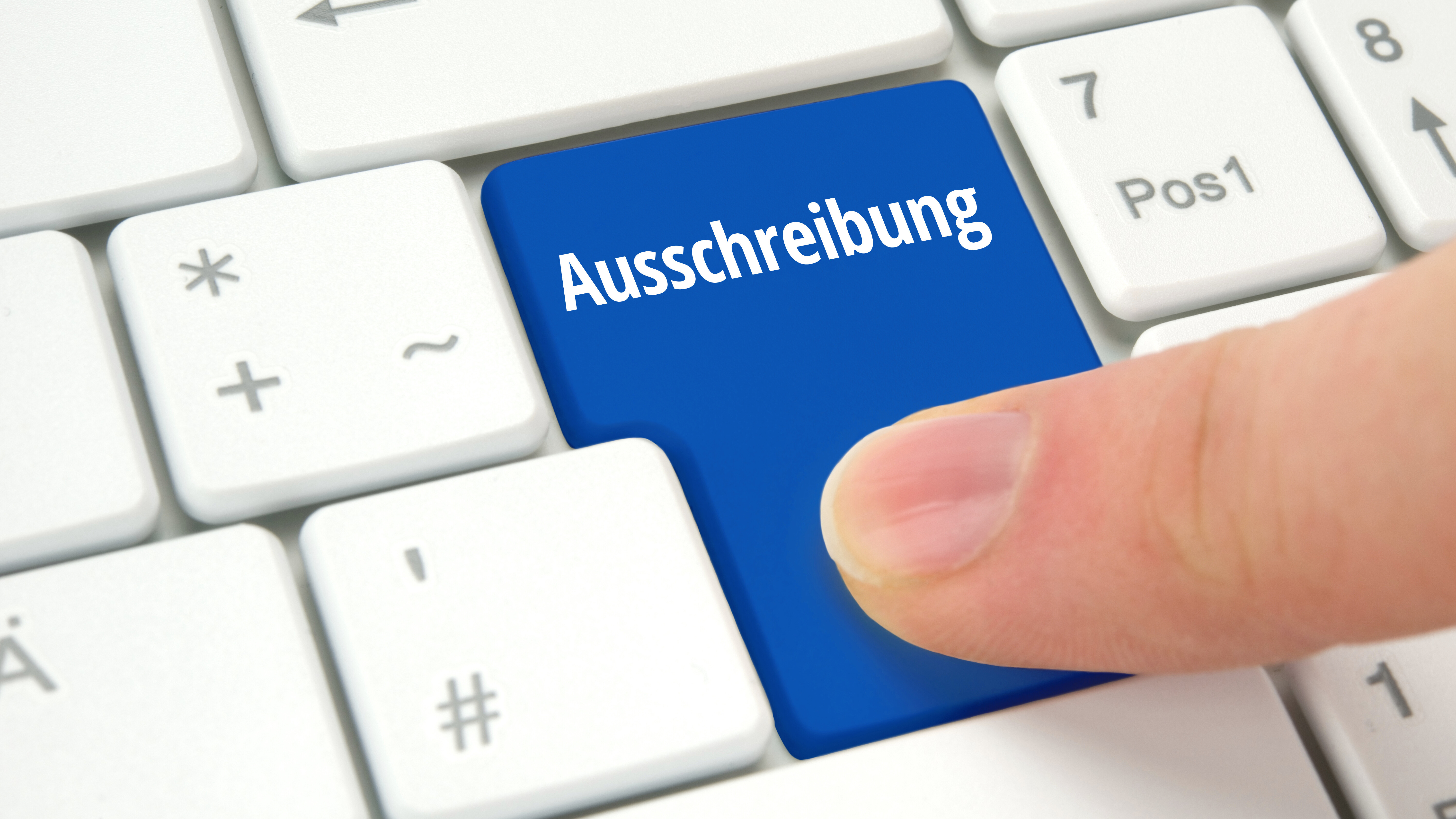Weiße Computertastatur mit einer blauen Enter-Taste im Vordergrund. Auf der Taste steht ‚Ausschreibung.