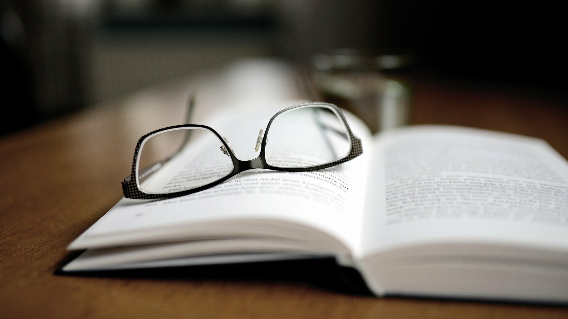 Ein aufgeklapptes Buch, auf dem eine Brille liegt.