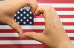 Zwei Hände bilden ein Herz, im Hintergrund ist die Flagge der USA.