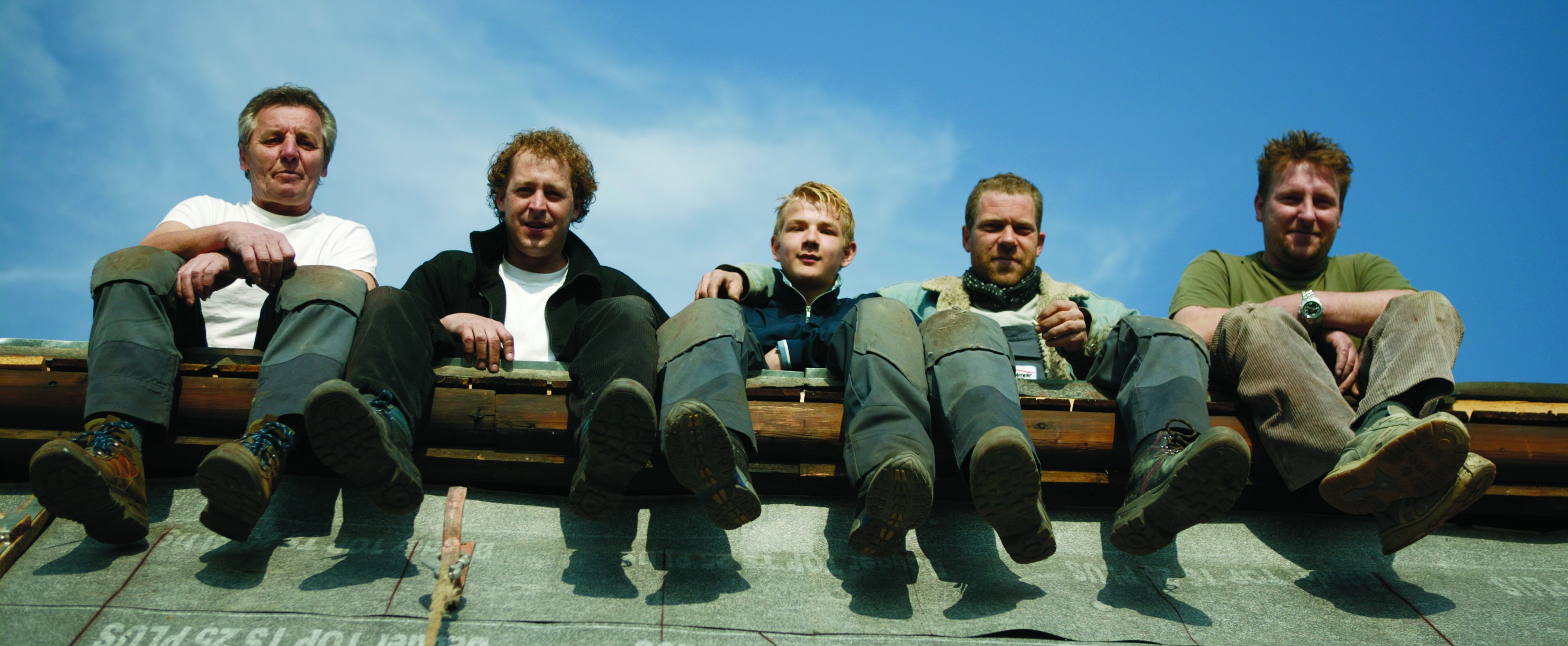 Fünf Männer sitzen auf einem Dach und blicken nach unten.