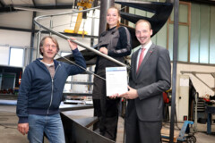 Ausbilder Holger Weiß (l.), Auszubildende Charissa van Willigenburg (Mitte) und Dirk Bleeker (r.) von der Handwerkskammer für Ostfriesland vor einer Spindeltreppe.
