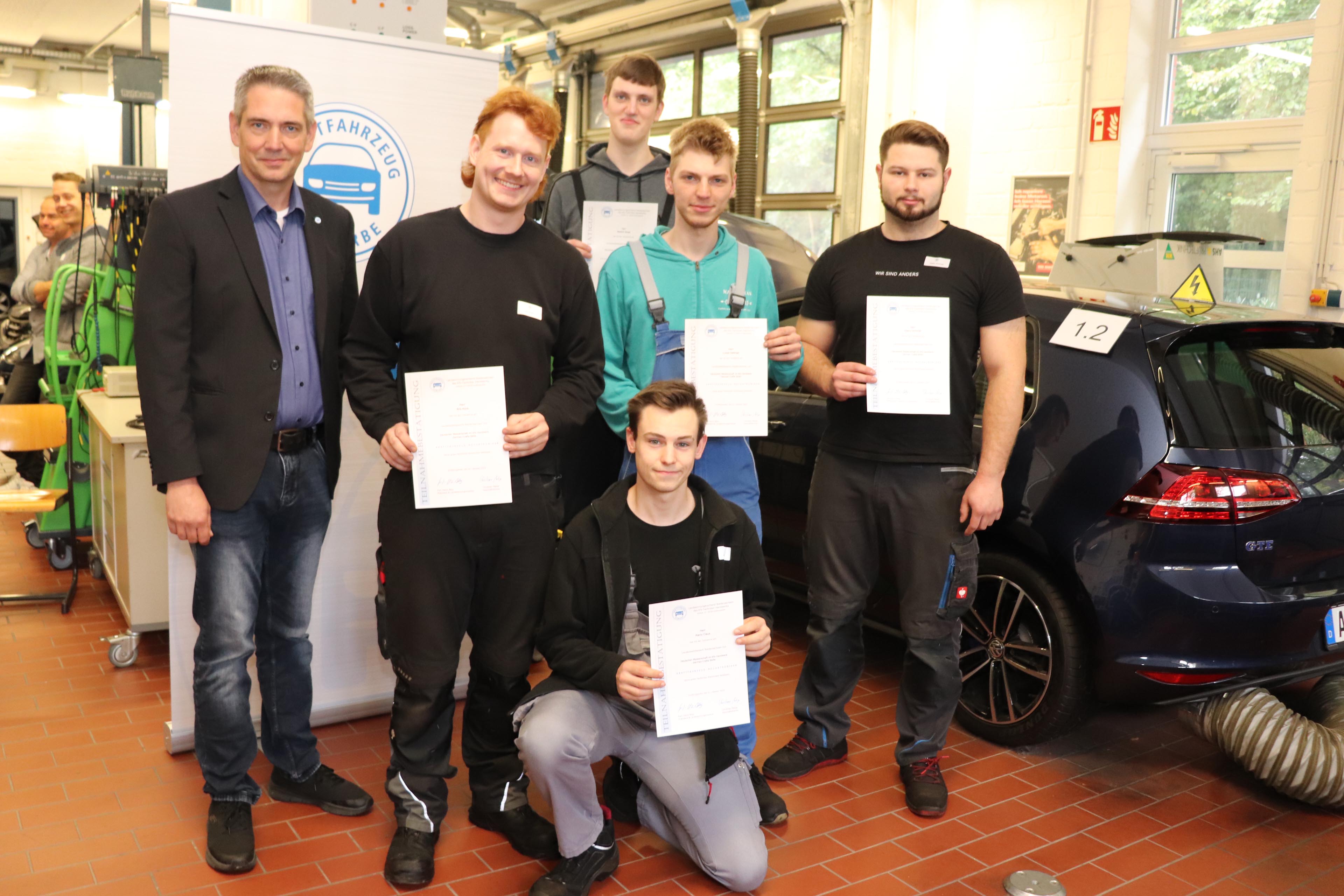 Zu sehen sind: Nils Kock aus Suddendorf (2.v.l., 1. Platz), Lukas Salenga aus Rhauderfehn (Mitte, 2. Platz), Matthis Braje aus Lohne (hinten, 3. Platz), Keanu Schmidt aus Nienburg (r., 4. Platz) und Mario Claus aus Rollshausen (vorne, 5. Platz) mit Thorsten Brändle (l.) vom Landesinnungsverband Niedersachsen des Kfz-Techniker-Handwerks.