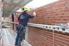 KI generiert: Eine Person in Arbeitskleidung reinigt eine Backsteinmauer auf einem Baugerüst.