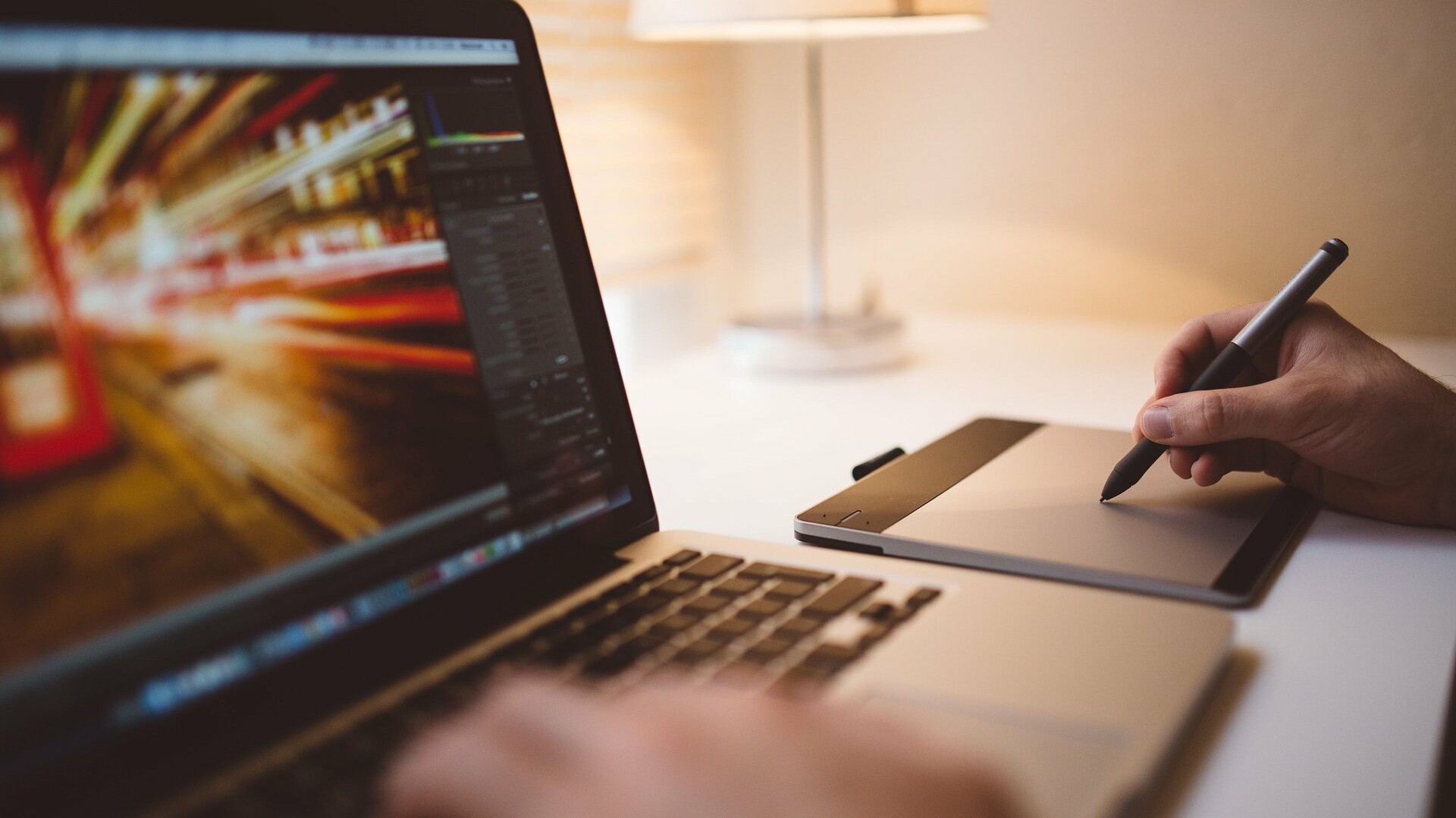 Jemand schreibt auf einem Laptop, daneben wird auf einem Zeichenpad gezeichnet.