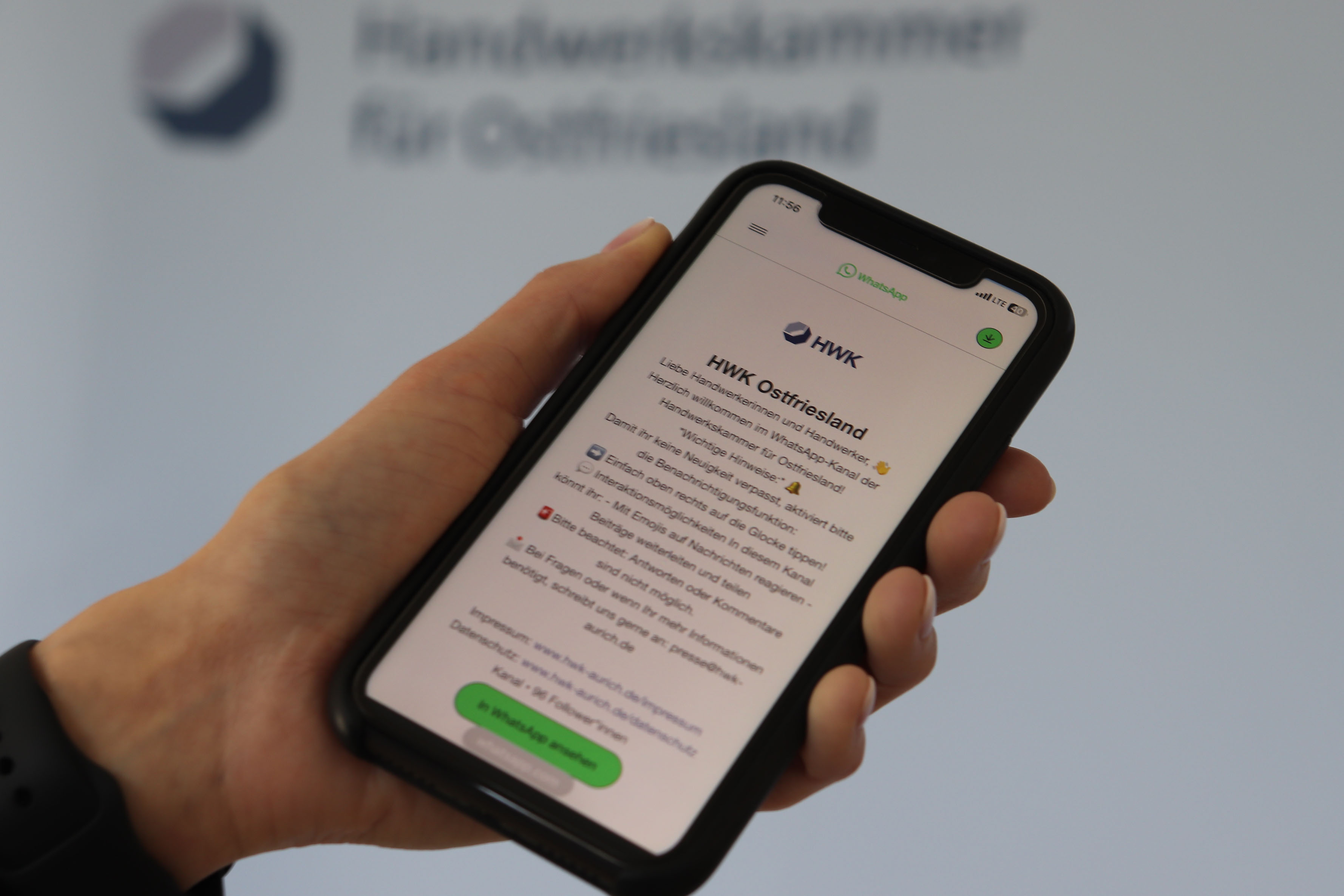 KI generiert: Eine Person hält ein Smartphone, das eine Nachricht der Handwerkskammer Ostfriesland auf WhatsApp anzeigt.