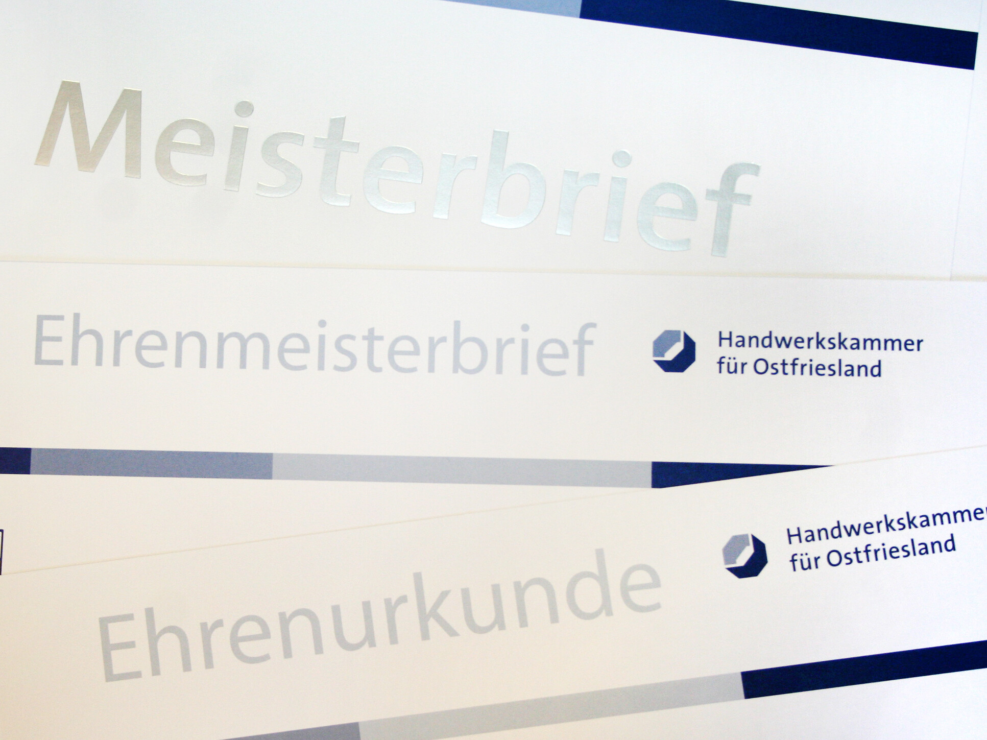 Einige Meisterbriefe und Ehrenurkunden liegen verteilt über das ganze Bild.