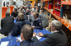 Innungsmitglieder sitzen an Tischen und hören einem Redner zu.