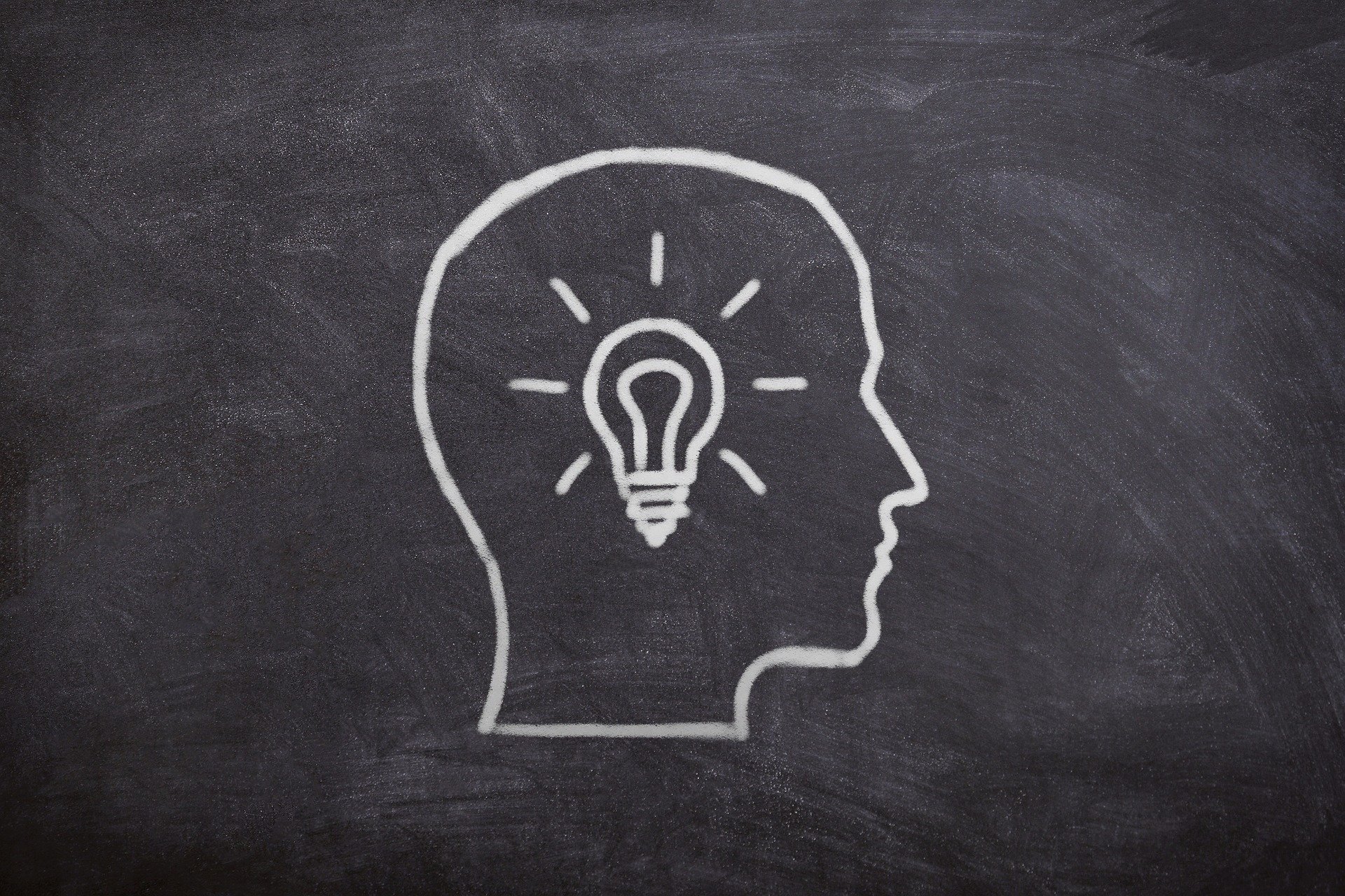 Mit Kreide gezeichneter Kopf auf einer Tafel, im Inneren des Kopfs eine Glühbirne – Symbol für Ideen oder Kreativität.