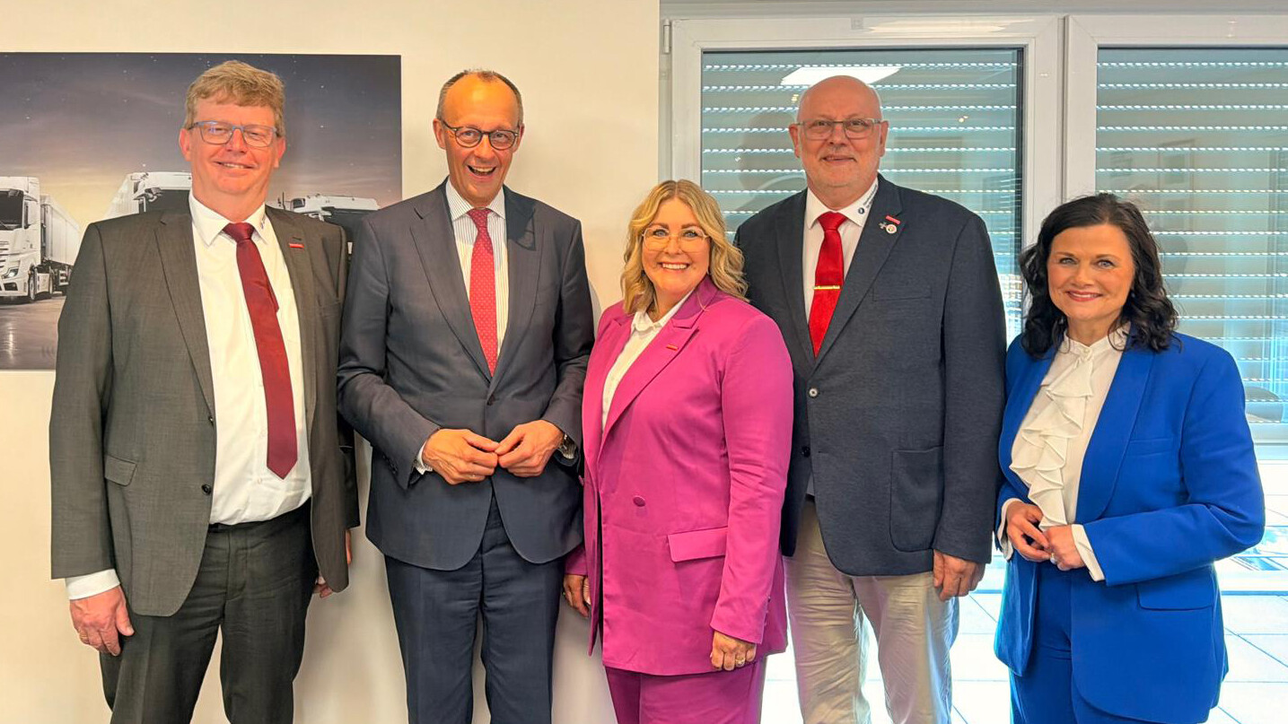 KI generiert: Eine Gruppe von fünf Personen in formeller Kleidung posiert gemeinsam für ein Foto vor einem Bürohintergrund.