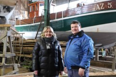 KI generiert: Das Bild zeigt zwei Personen in Winterkleidung vor einem in einer Halle befindlichen Boot.