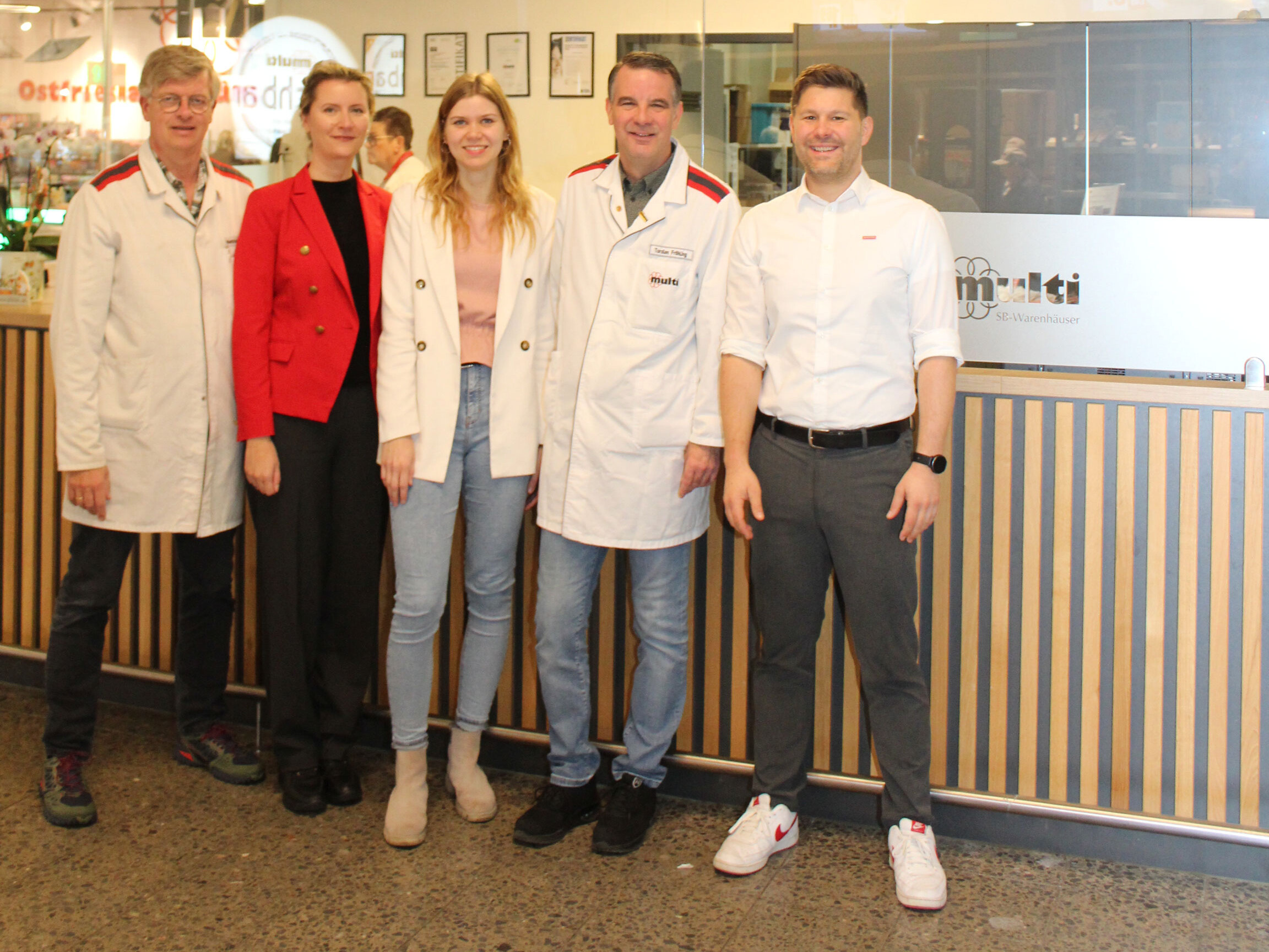 KI generiert: Das Bild zeigt fünf Personen, die vor einem Gebäude mit gelben Türen und einem Schild mit der Aufschrift "OSTFRIESLAND" stehen und lächeln.