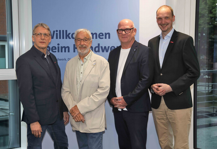 KI generiert: Das Bild zeigt vier Männer, die vor einem Schild mit der Aufschrift "Willkommen beim Handwerk" stehen.