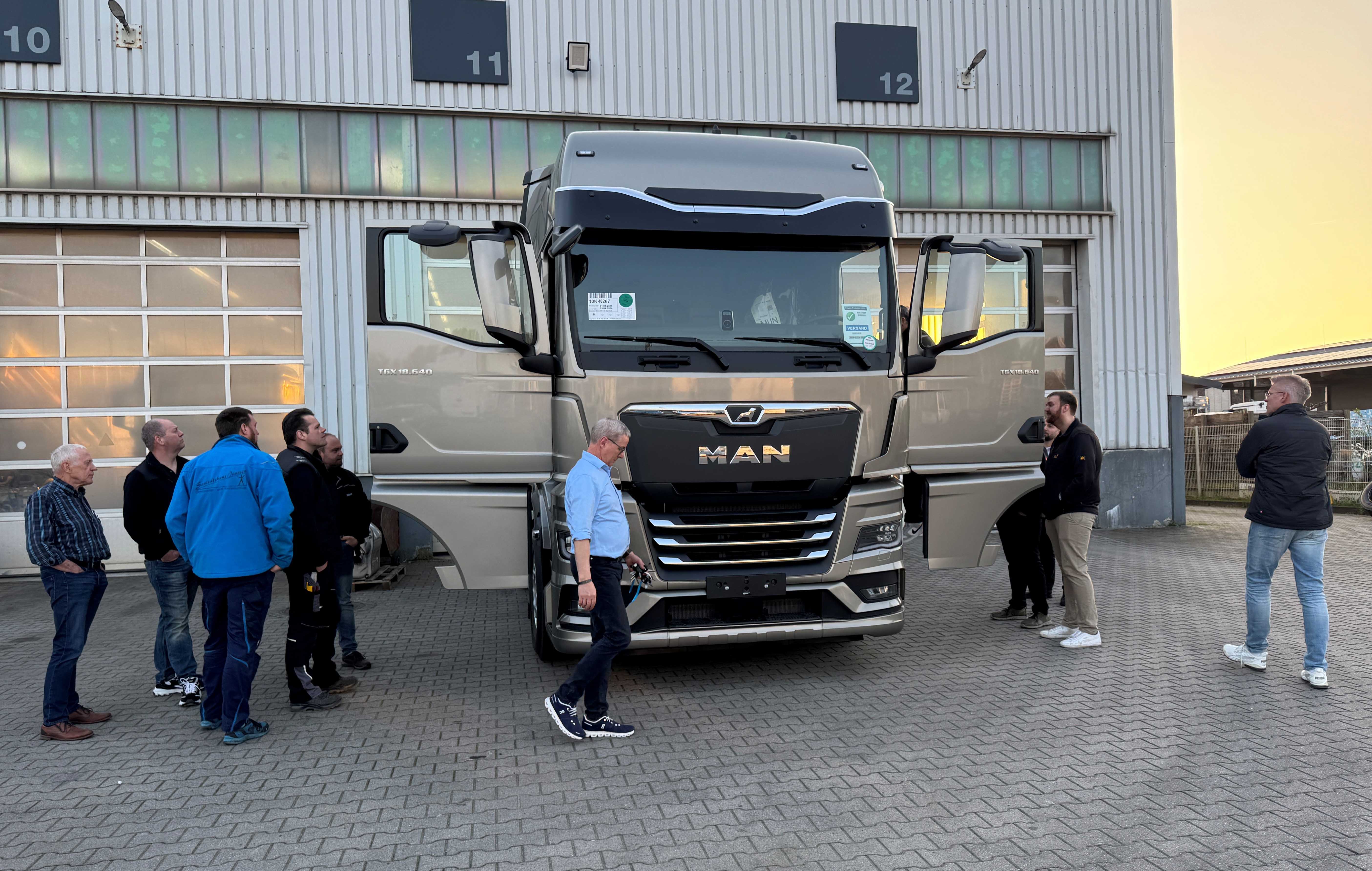 KI generiert: Eine Gruppe von Menschen betrachtet einen großen MAN-LKW vor einer Halle.