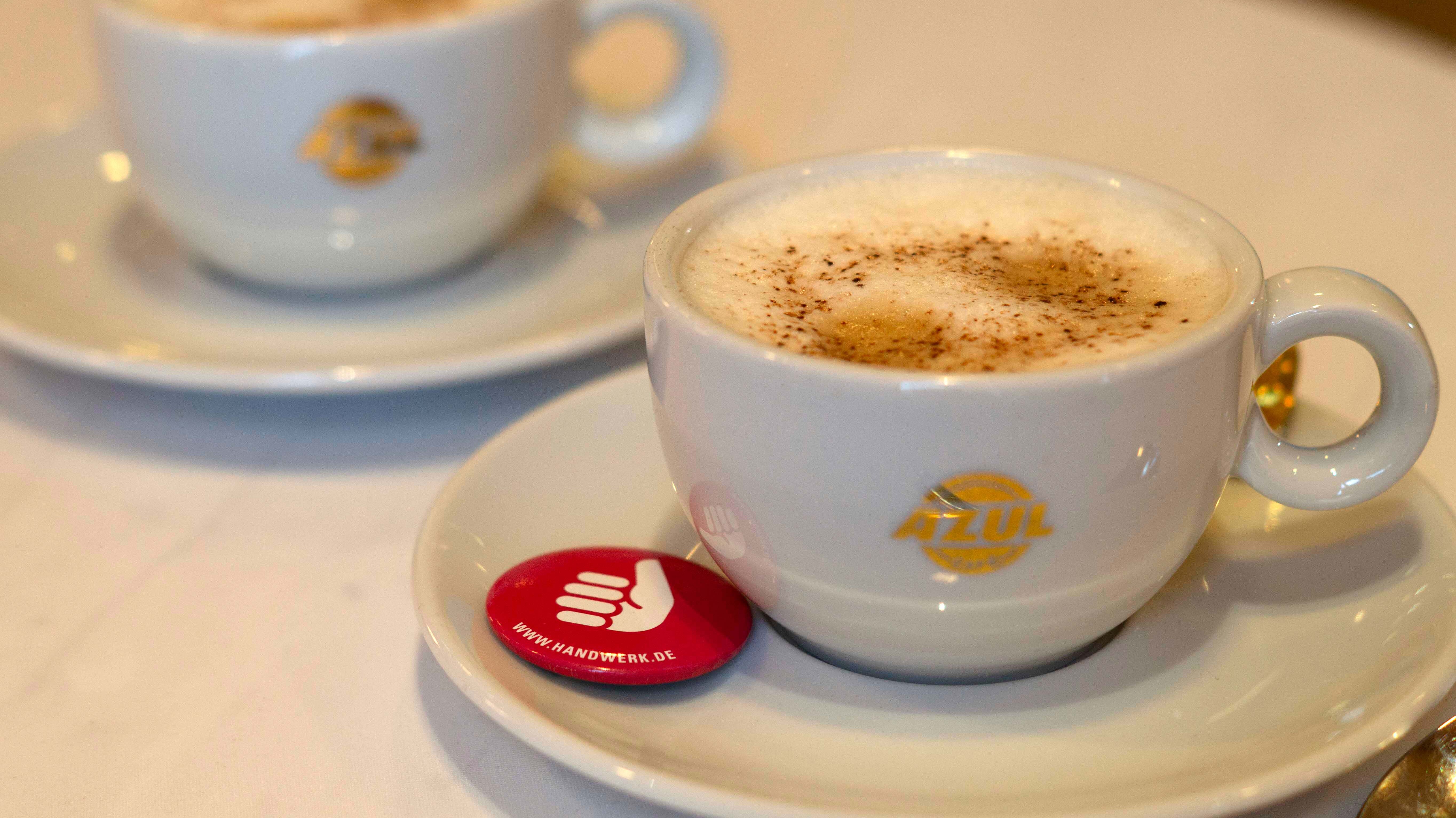 Zwei Tassen Kaffee und ein kleiner Anstecker der Handwerkskammer.