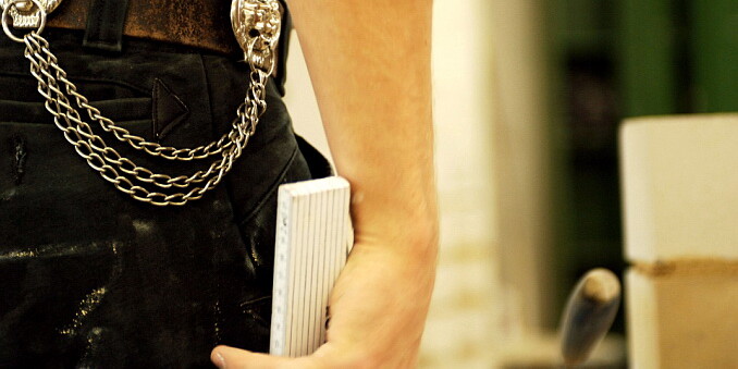 KI generiert: Das Bild zeigt eine Person mit dunkler Hose, an der eine Kette mit Schädelmotiv befestigt ist, die ein Notizbuch in der Hand hält.
