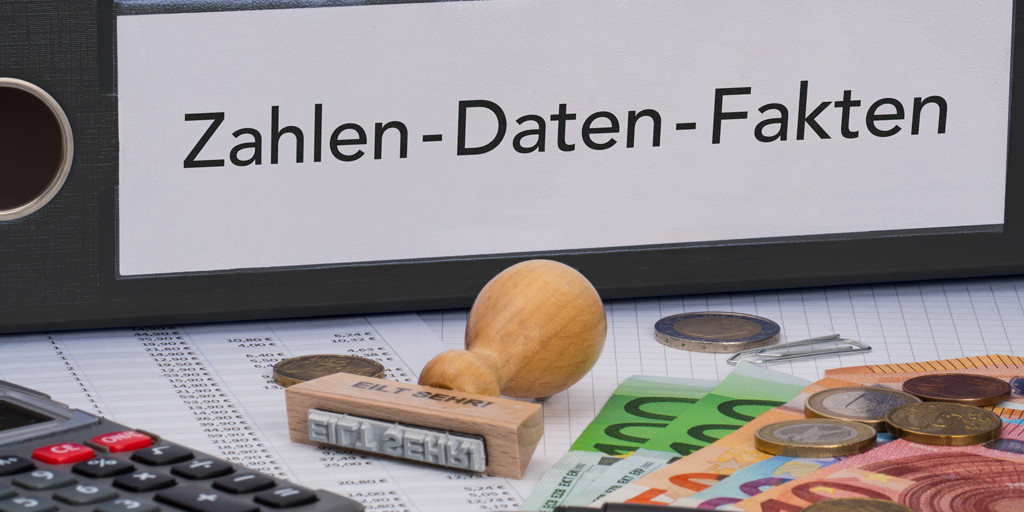 Ein Ordner mit der Aufschrift ‚Zahlen – Daten – Fakten‘. Davor liegen ein Stempel, ein Taschenrechner und Geld.