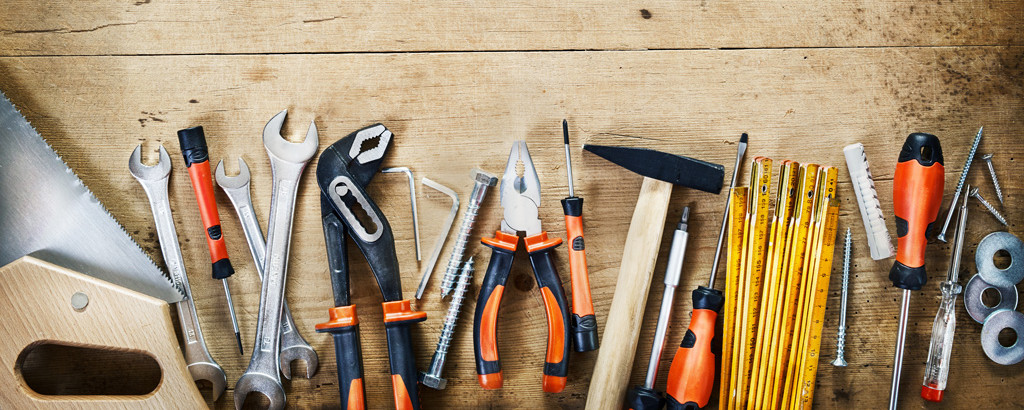 Viele verschiedene Werkzeuge liegen leicht durcheinander in einer Reihe – symbolisch für handwerkliche Tätigkeit und praktische Arbeit.