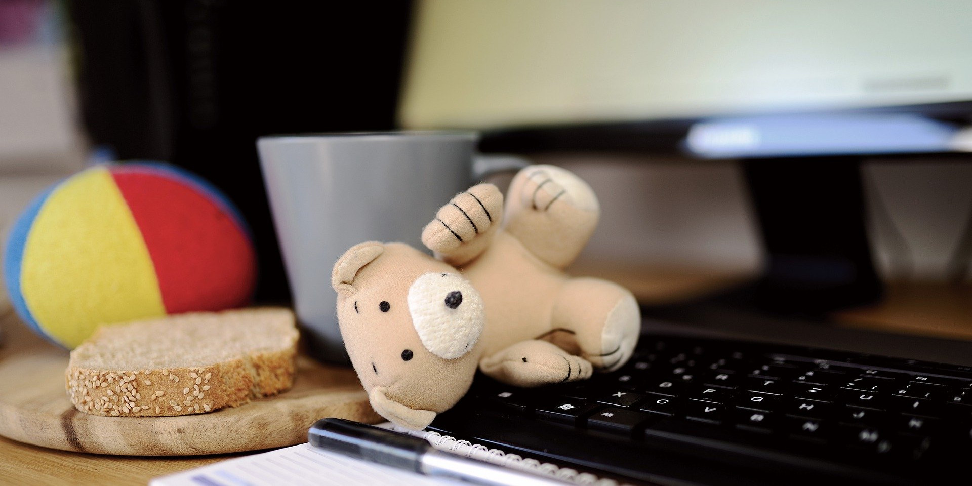 Ein PC mit Tastatur, auf der ein kleiner Teddybär liegt.