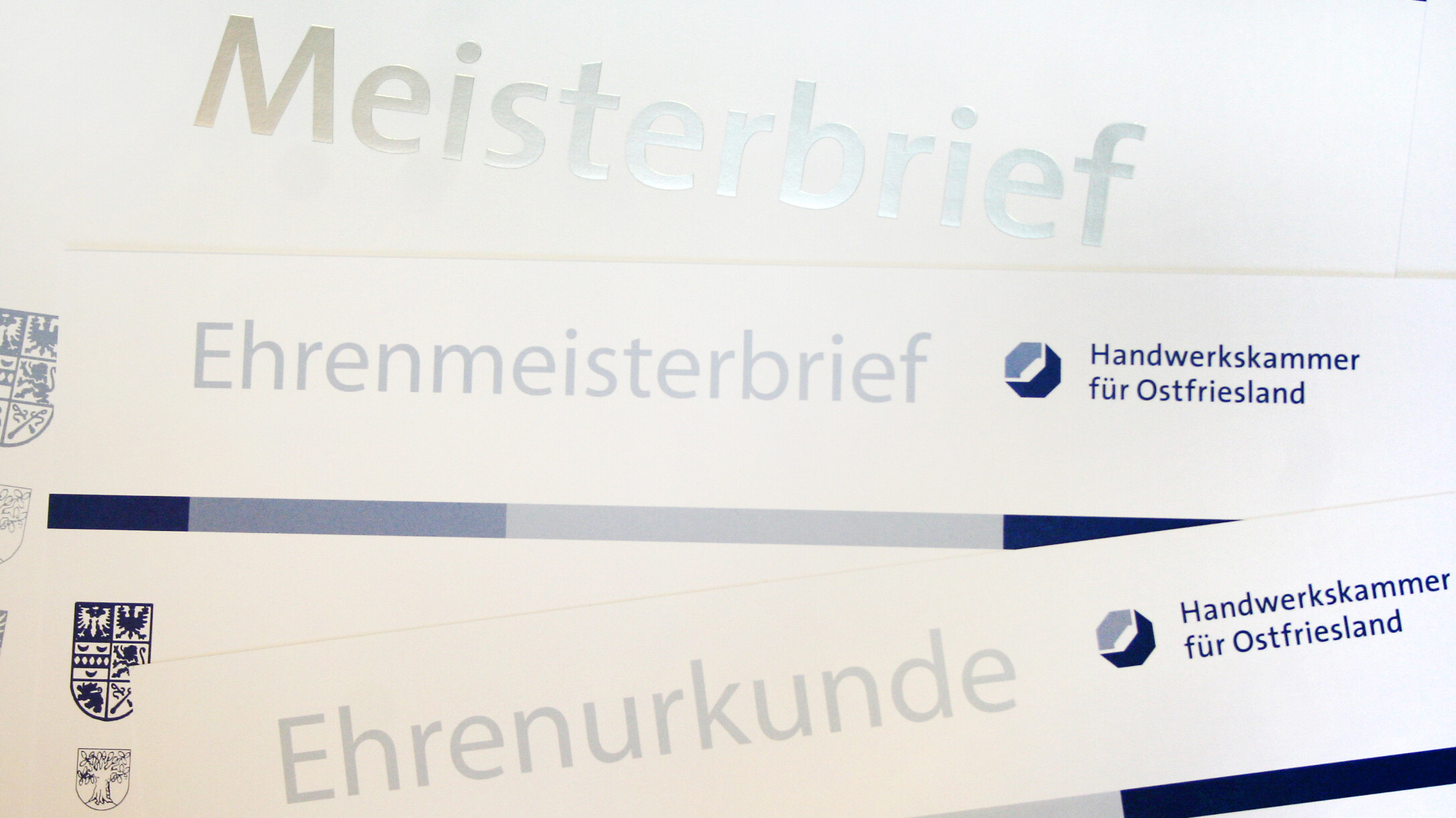 Einige Meisterbriefe und Ehrenurkunden liegen verteilt über das ganze Bild.