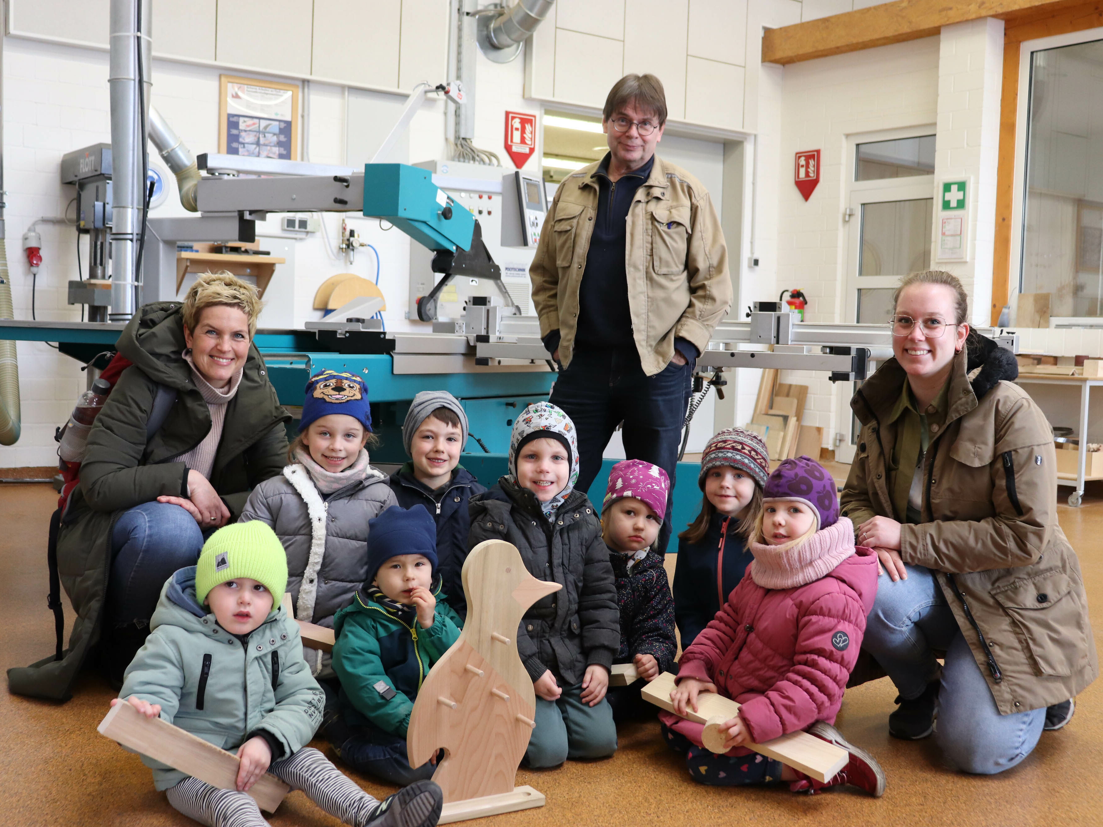 Lehrwerksmeister Uwe Herzich (hinten) machte der Tischler-Projektgruppe des Pinguin Kindergartens und den beiden Erzieherinnen Mieke Mathes (l.) und Lea Krüger-Kortum (r.) ein ganz besonderes Geschenk: Ein Vogel aus Holz. 