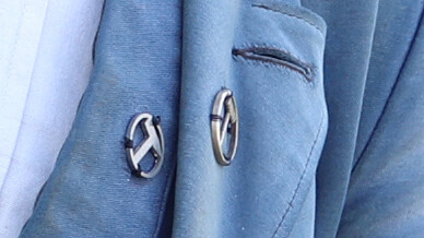 KI generiert: Das Bild zeigt das Revers eines blauen Blazers mit zwei dekorativen Reversnadeln oder Abzeichen.
