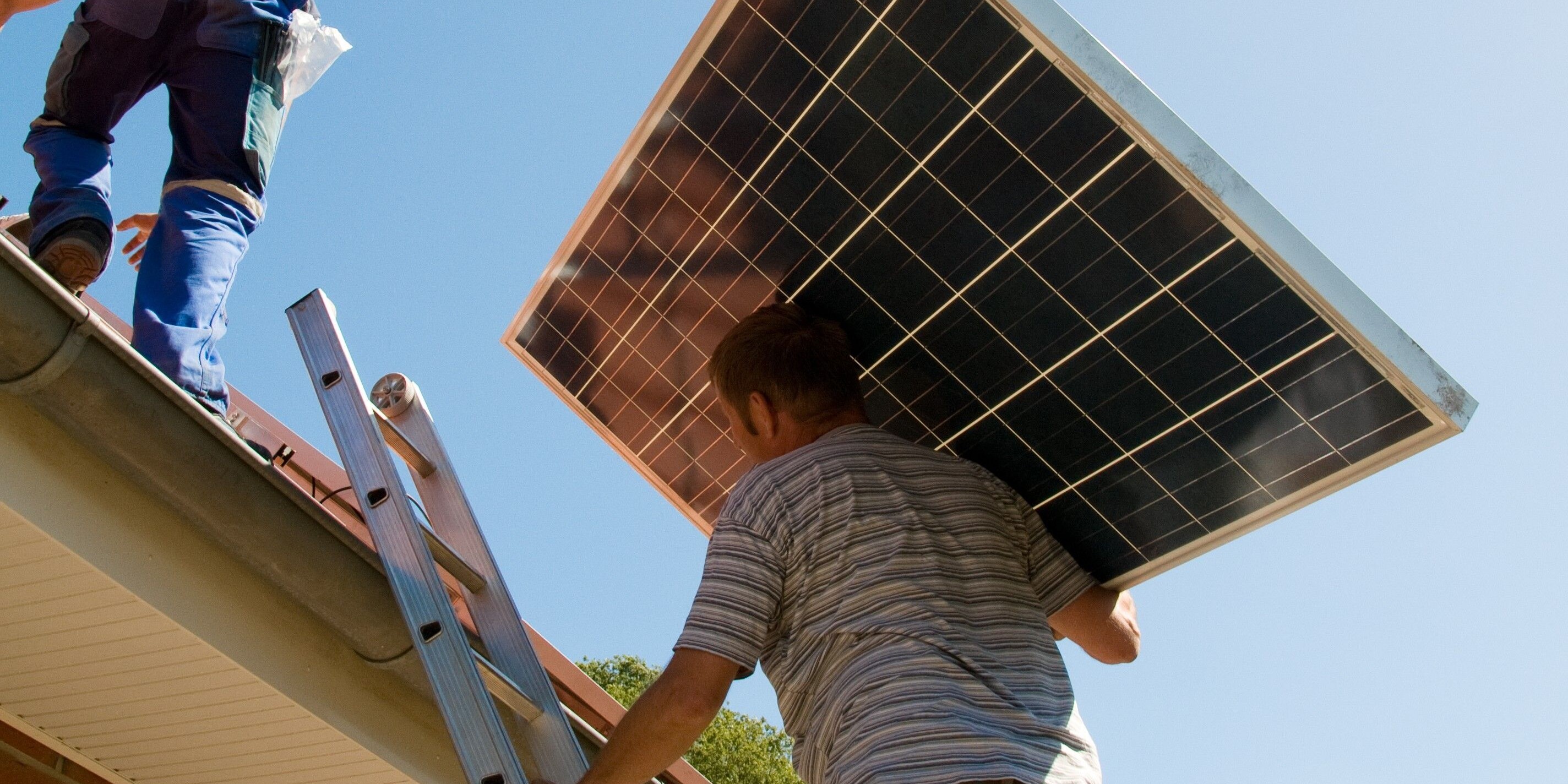 Mit kräftigen Händen trägt ein Mann ein Solarpanel auf das Dach – ein Schritt in Richtung nachhaltiger Energie.