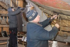 KI generiert: Das Bild zeigt zwei Personen, die an einem Bootsrumpf arbeiten.