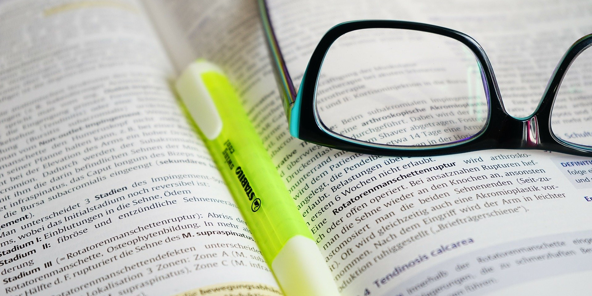 Ein aufgeklapptes Buch mit einem Marker in der Mitte und einer Brille auf der rechten Seite.