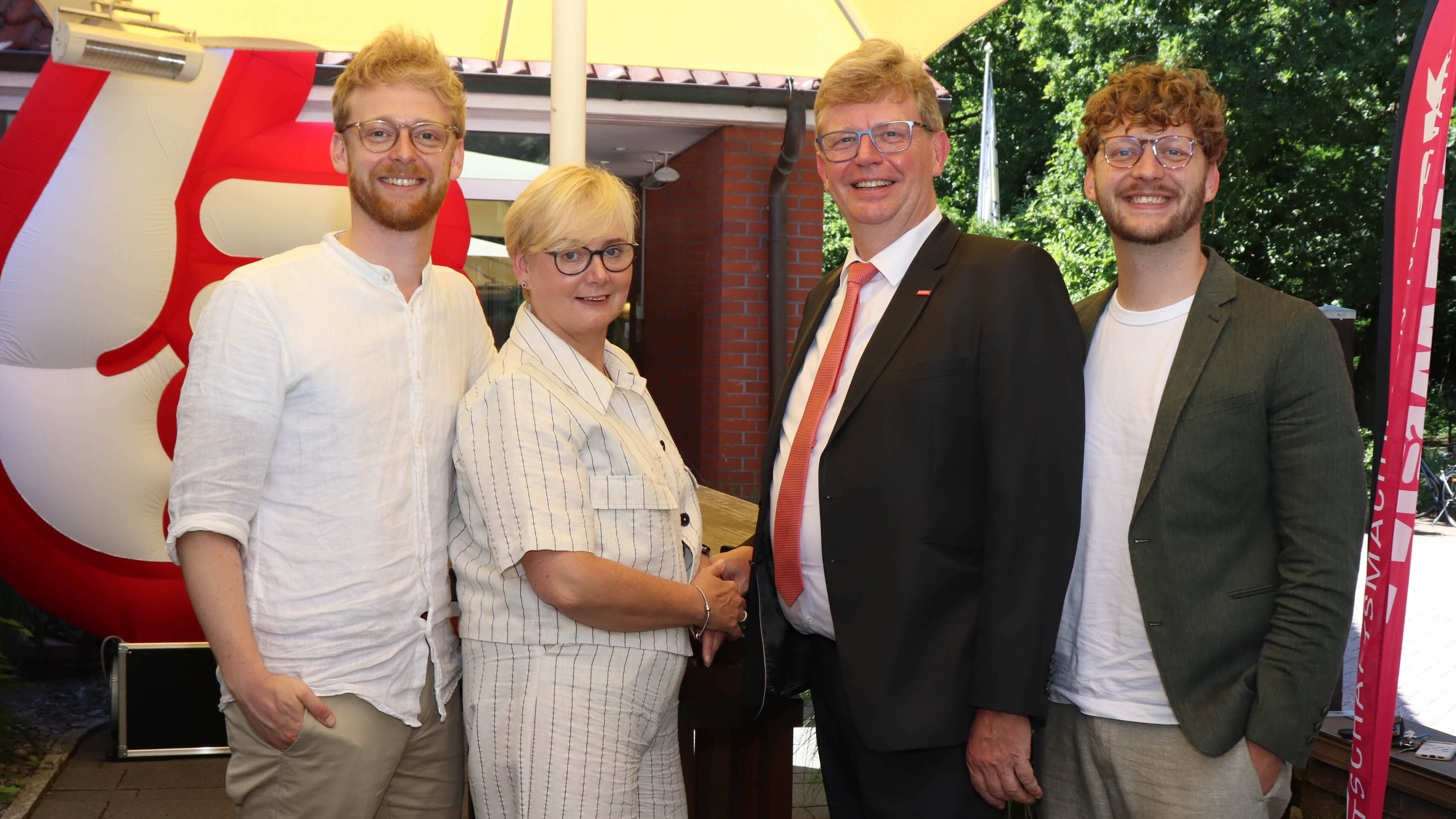 KI generiert: Auf dem Bild sind vier Personen vor einem roten Hintergrund, die fröhlich in die Kamera schauen.