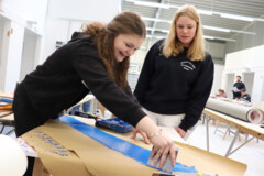 KI generiert: Zwei Personen arbeiten zusammen an einem Tisch an einem kreativen Projekt, bei dem blaue Farbe auf Papier aufgetragen wird.