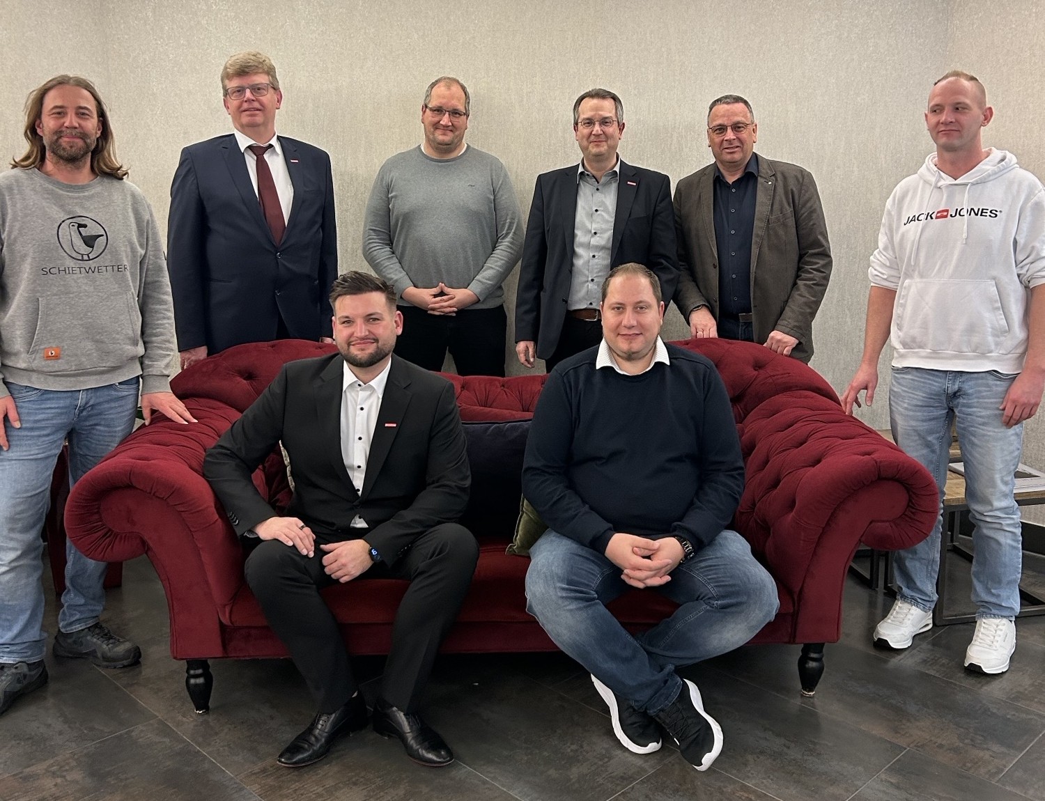 KI generiert: Eine Gruppe von acht Männern posiert vor und auf einem roten Sofa für ein Gruppenfoto.