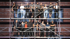 Vor einer Hausfassade auf einem Gerüst stehen  mehrere Handwerker.