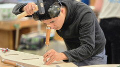 KI generiert: Ein junger Mann arbeitet konzentriert mit einem Stechbeitel an einem Holzstück.