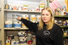 KI generiert: Eine Person steht vor einem Regal voller Farb- und Lackdosen.