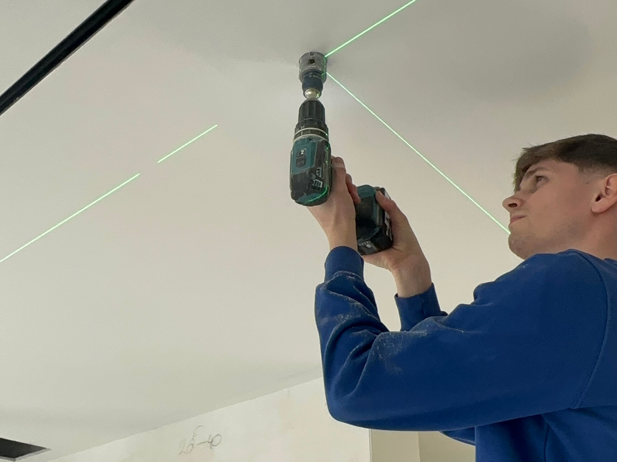 KI generiert: Eine Person verwendet eine Bohrmaschine, um an der Decke zu arbeiten, während ein grüner Laser zur Ausrichtung dient.
