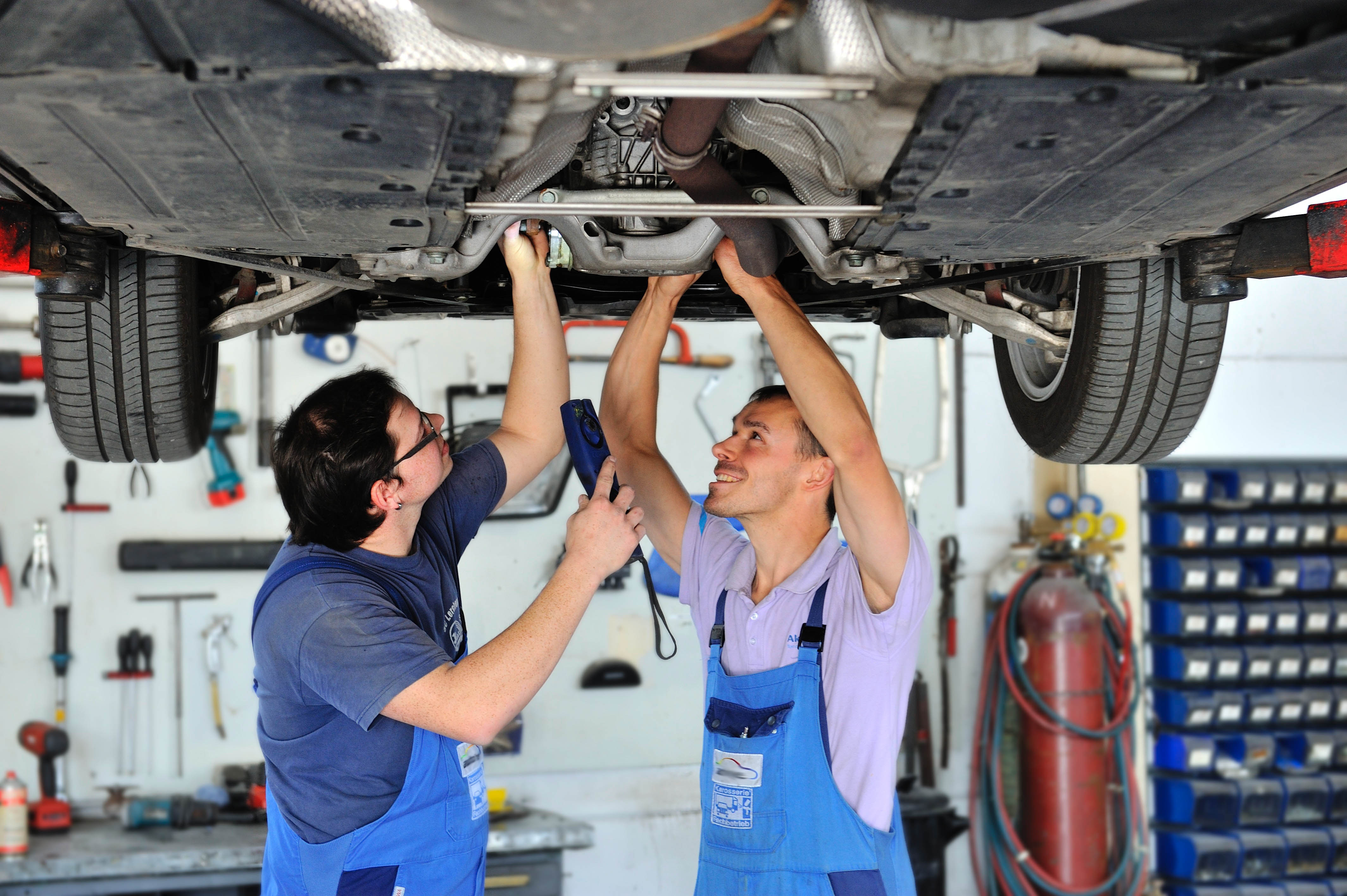 Zwei Kfz-Handwerker arbeiten zusammen unter einem Auto.